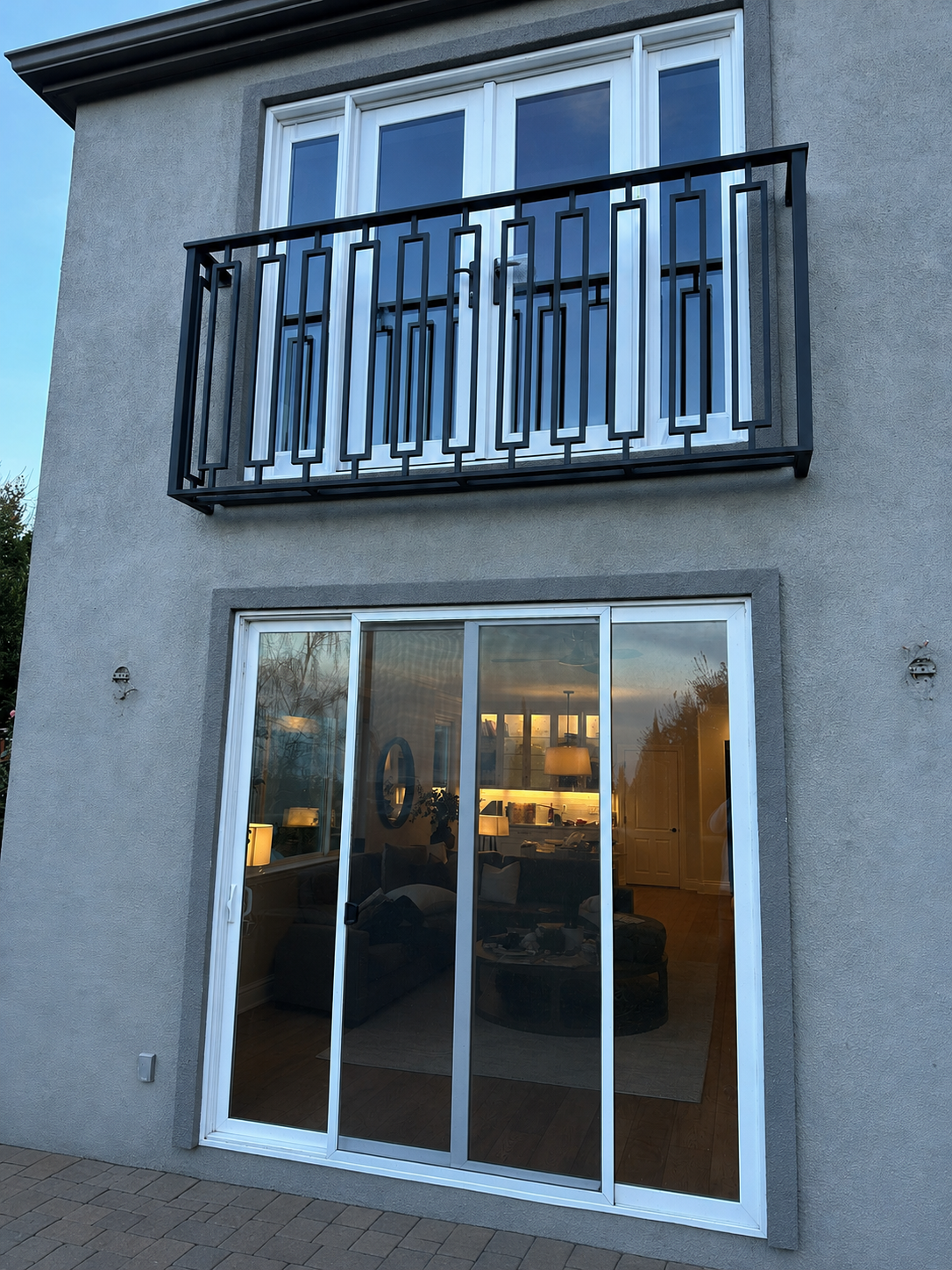 Gray stucco home with black geometric balcony railing above glass patio doors