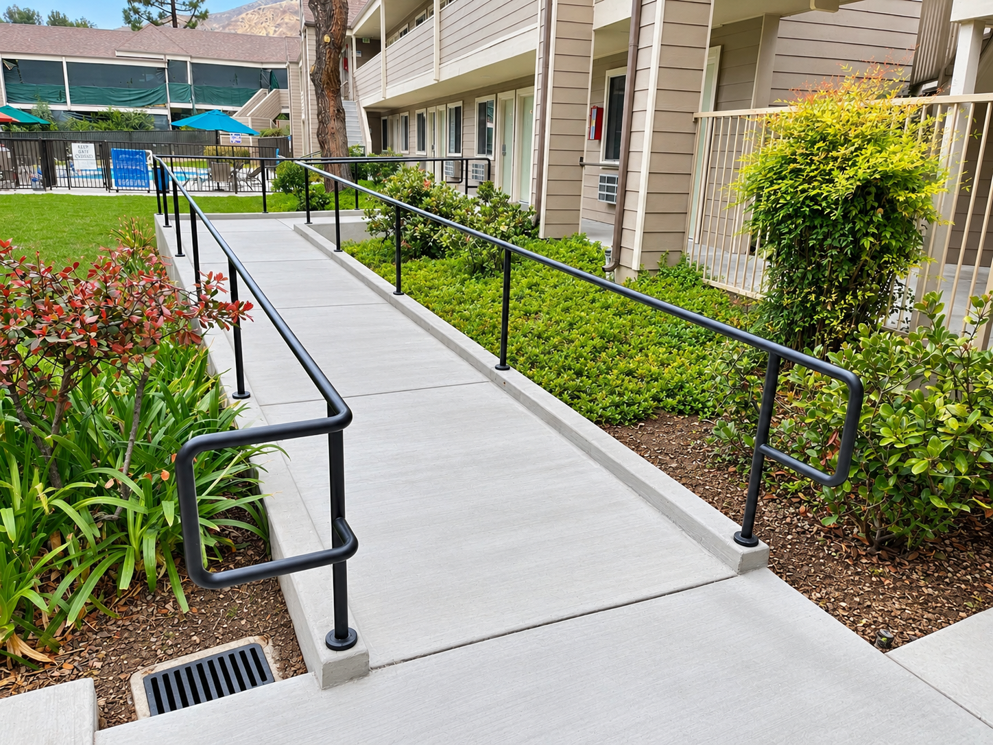 Commercial accessibility ramp with black handrails through landscaped courtyard