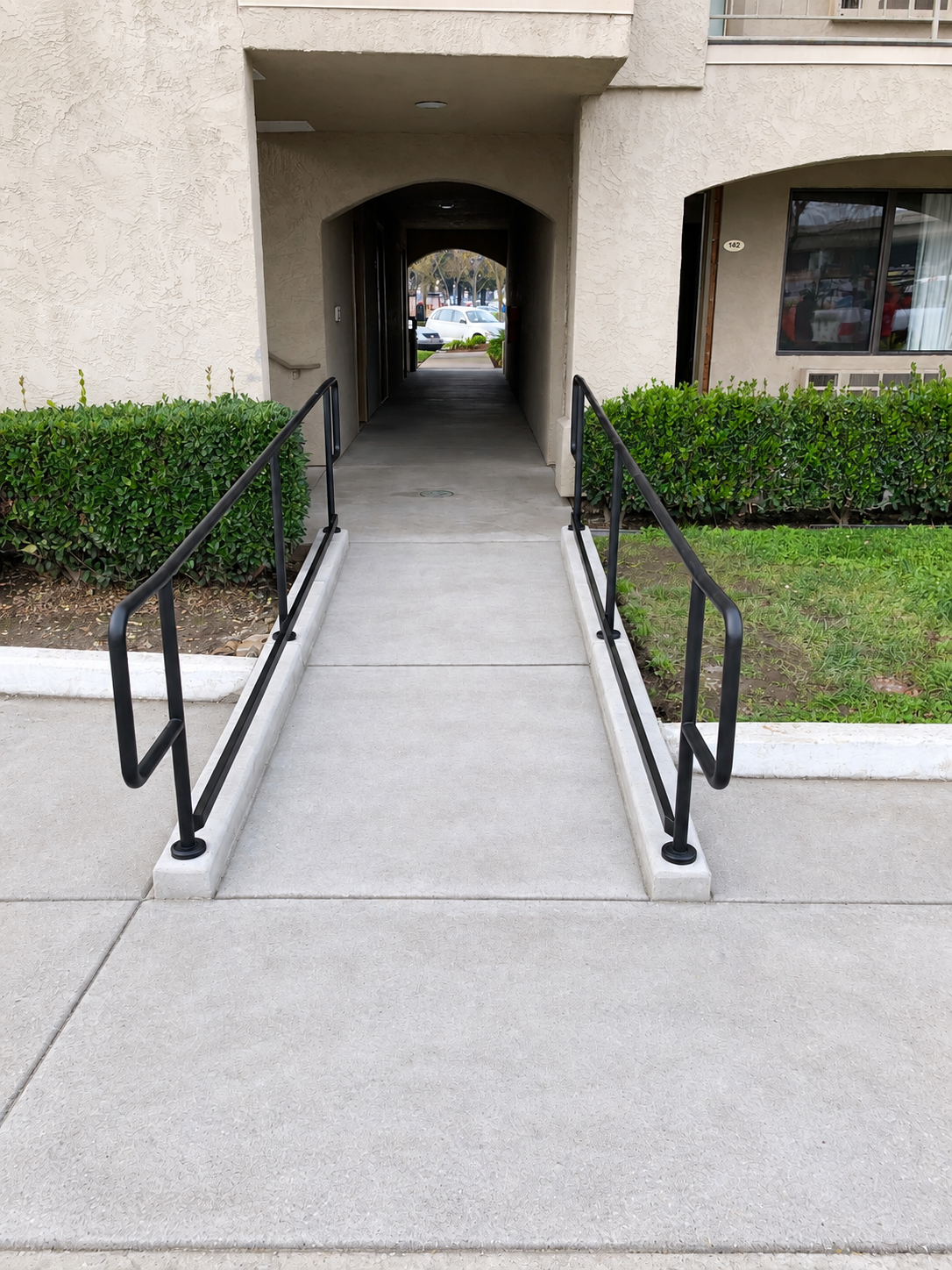 Commercial entry ramp with black handrails leading through apartment breezeway