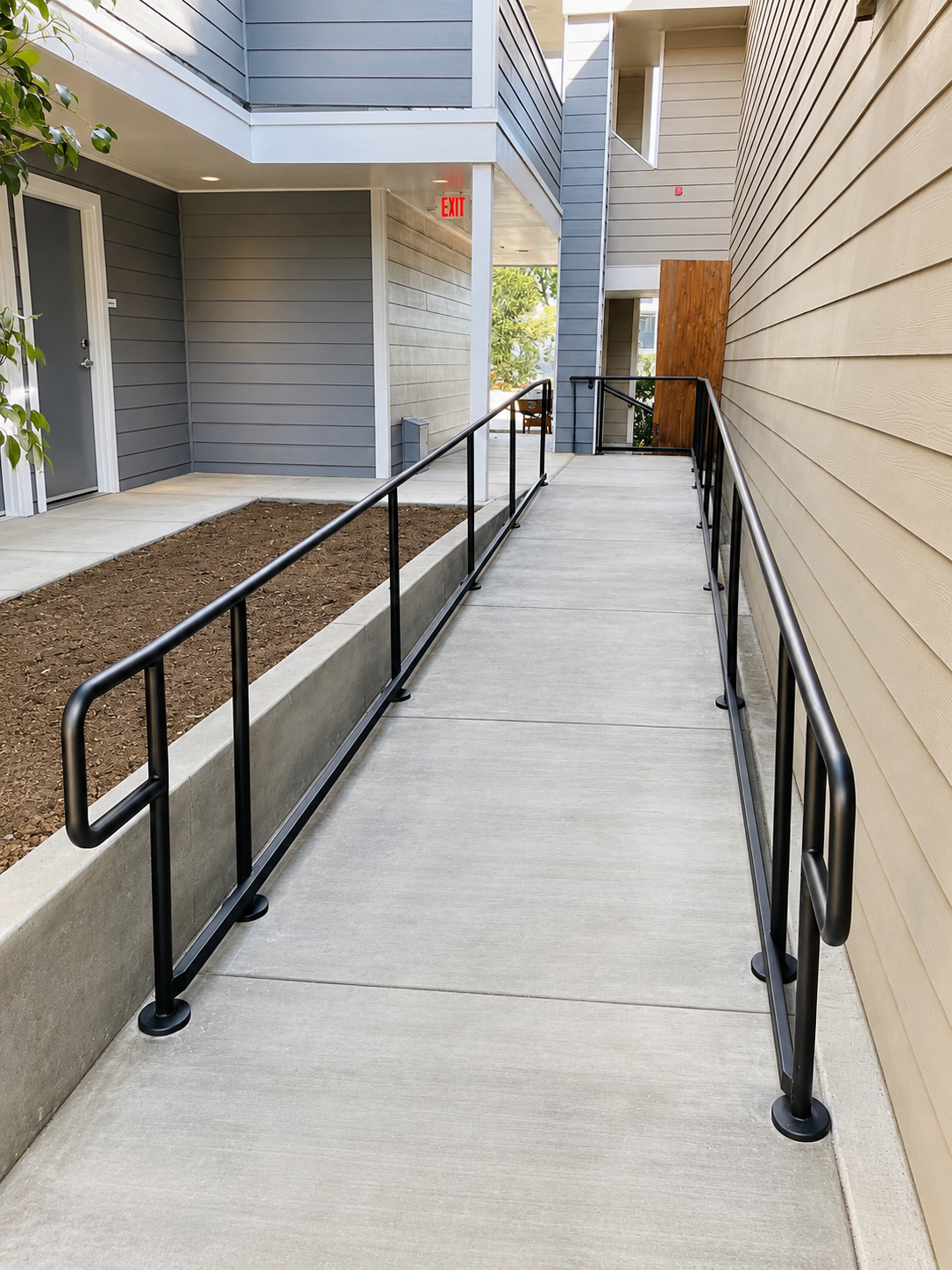 Commercial walkway ramp with black handrails beside apartment siding