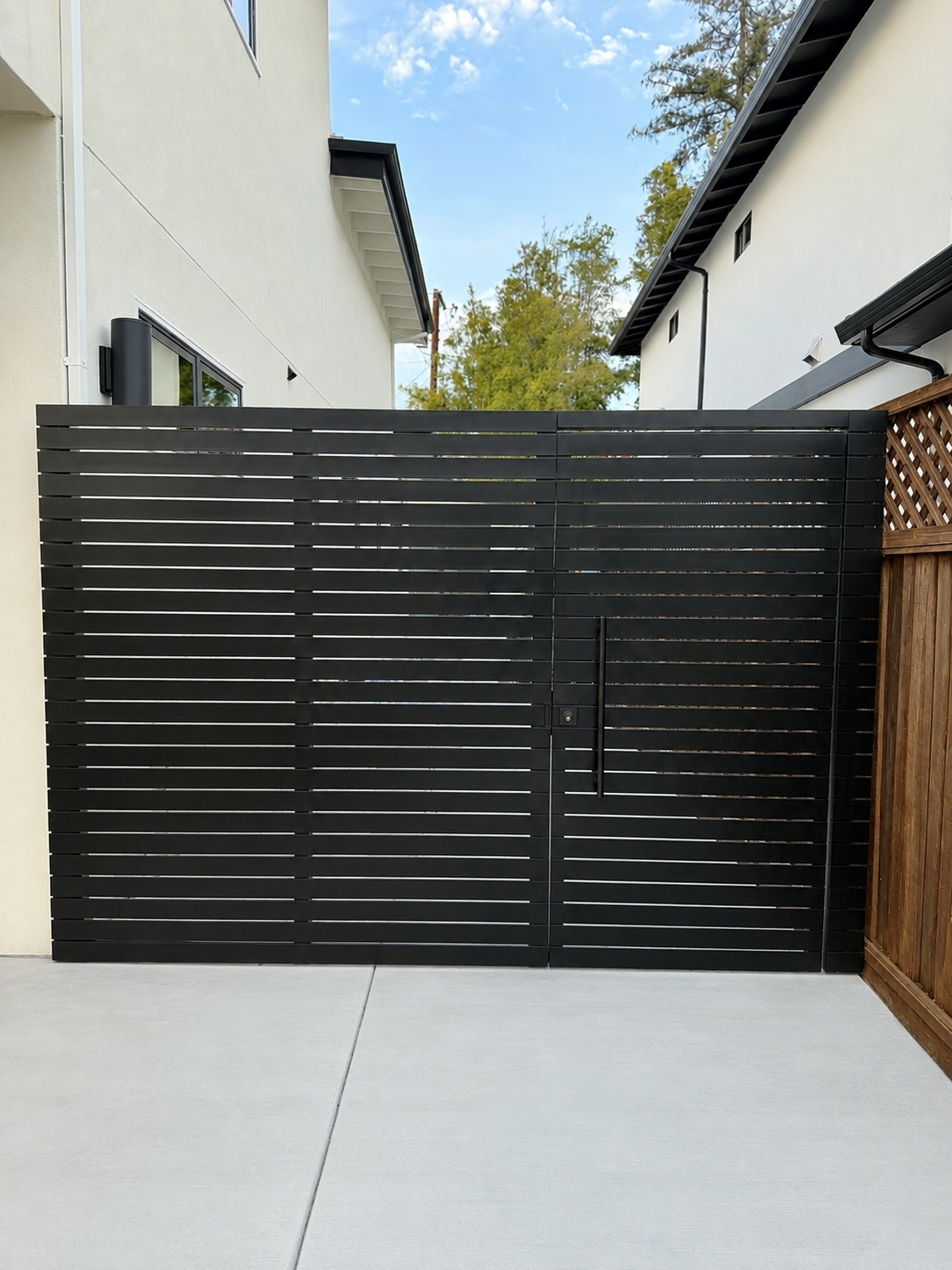 Black horizontal slat side gate between white homes