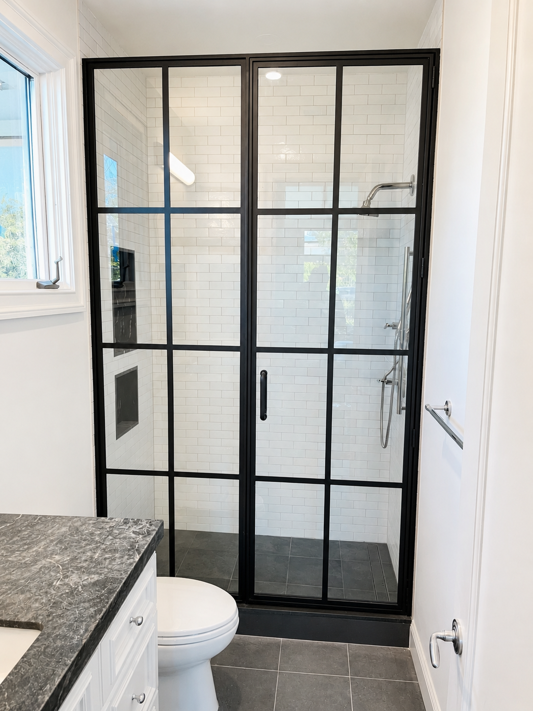 Black metal and glass shower enclosure with white tile walls