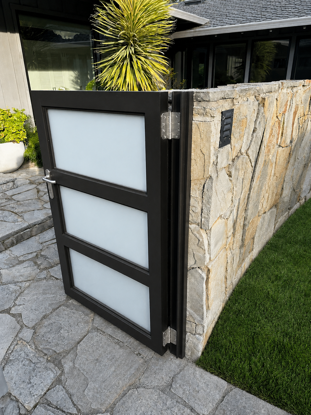 Close view of black metal frosted glass gate with stone wall