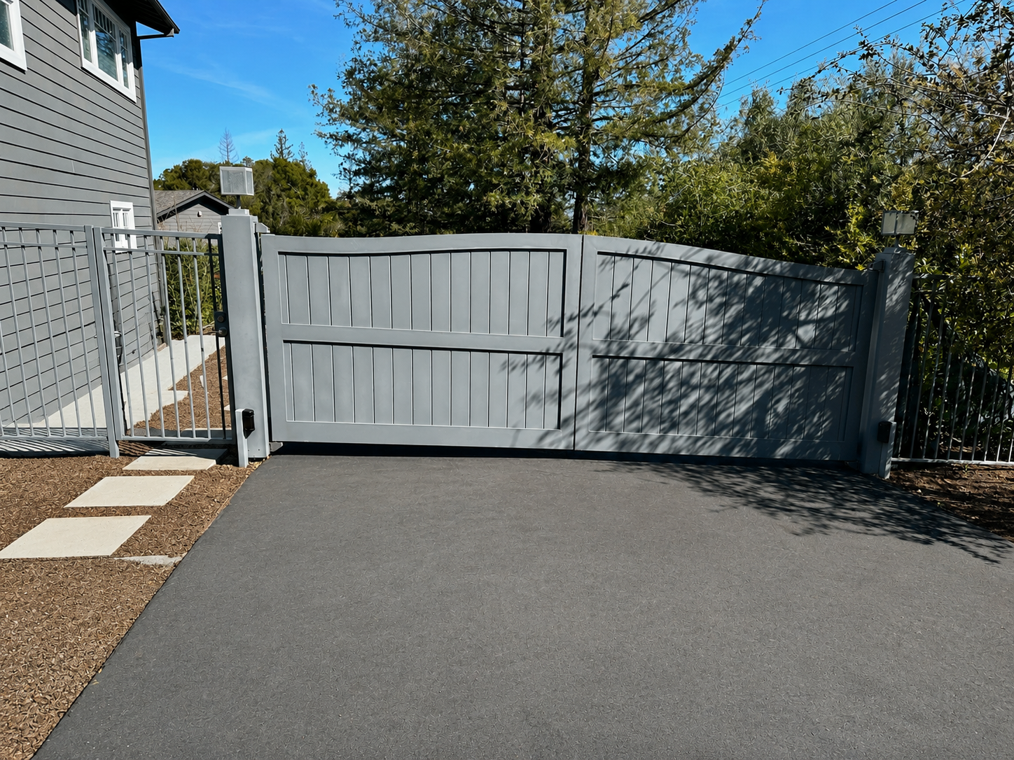 Wide view of gray driveway gate with matching side fence and pedestrian gate