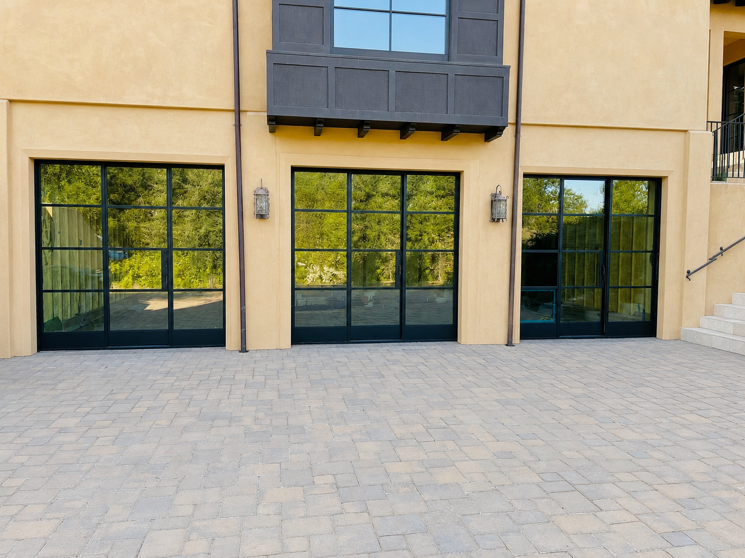 Wide exterior view of black grid glass doors across a stucco home facade
