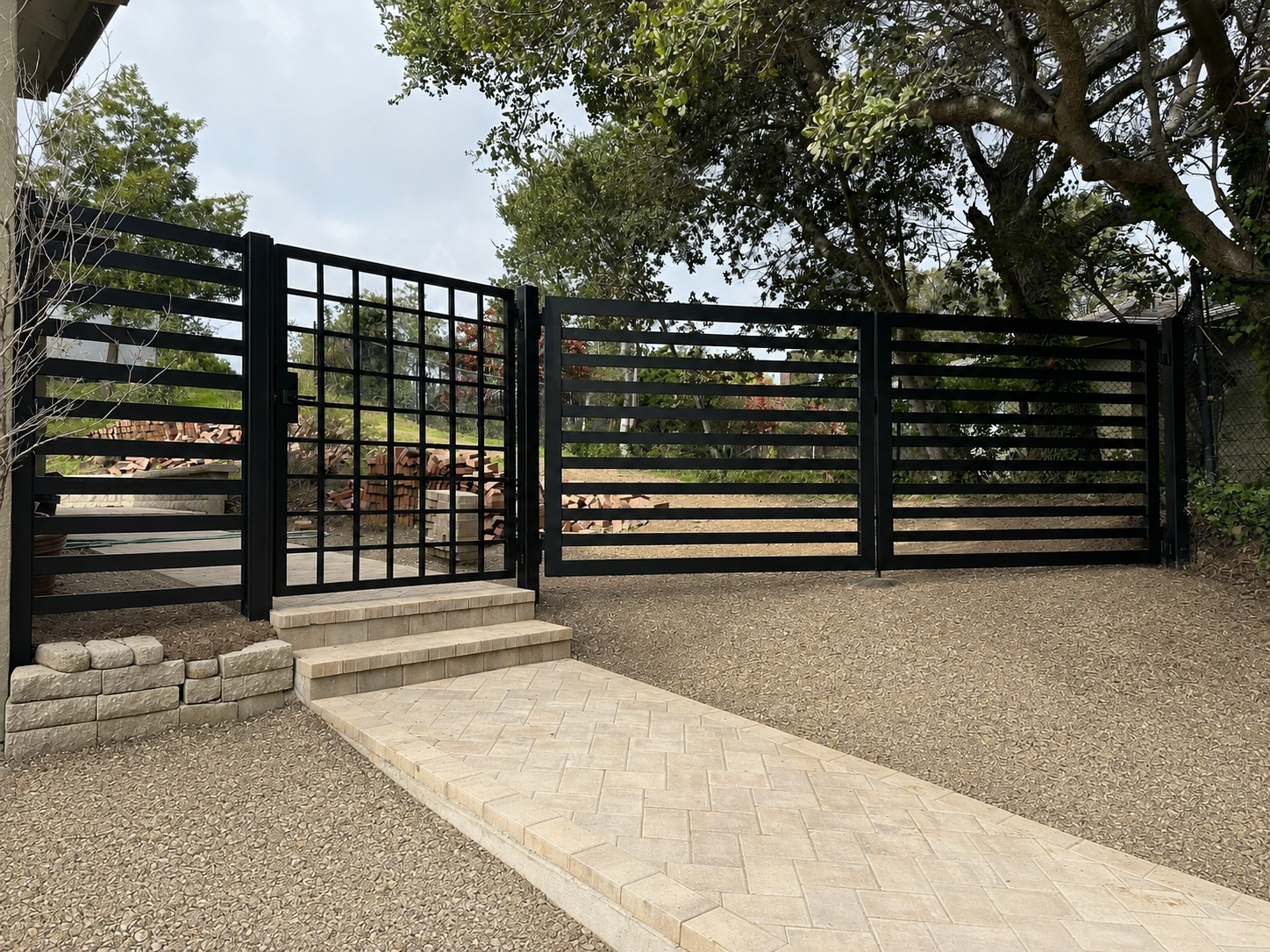 Black hillside driveway gate with horizontal bars and grid pedestrian gate
