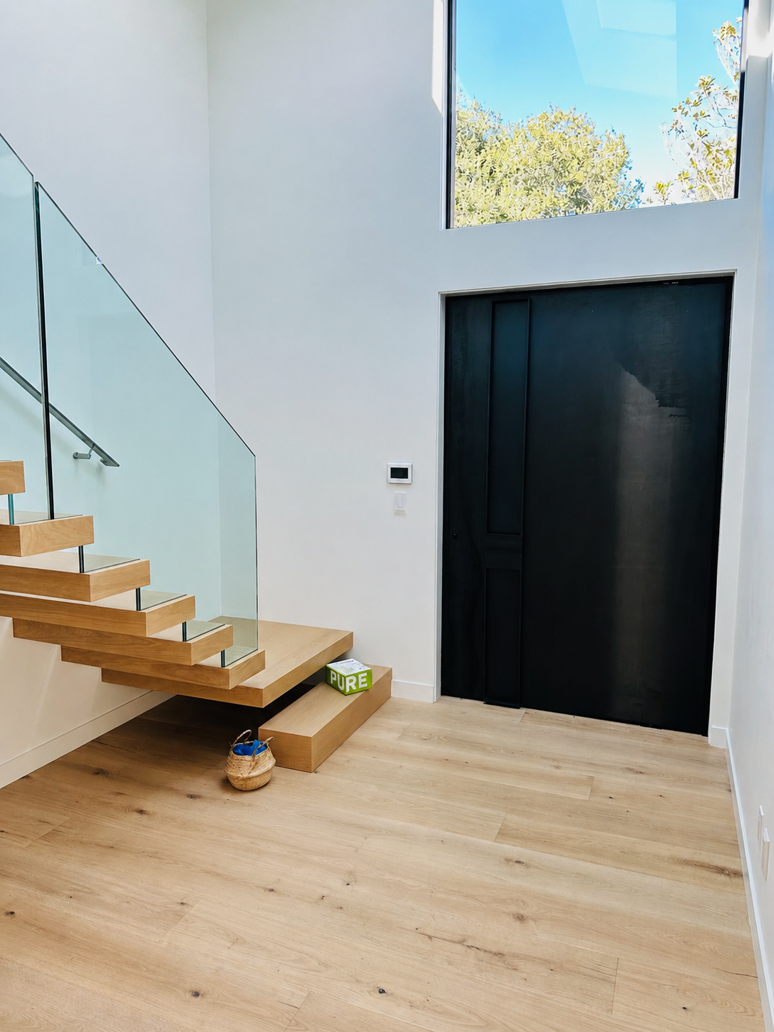 Modern black steel pivot door beside floating wood stairs and glass railing