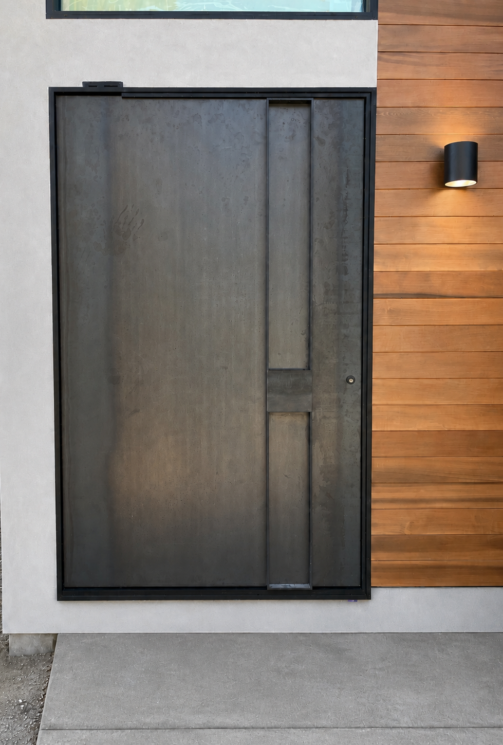 Exterior view of black steel pivot door beside wood siding