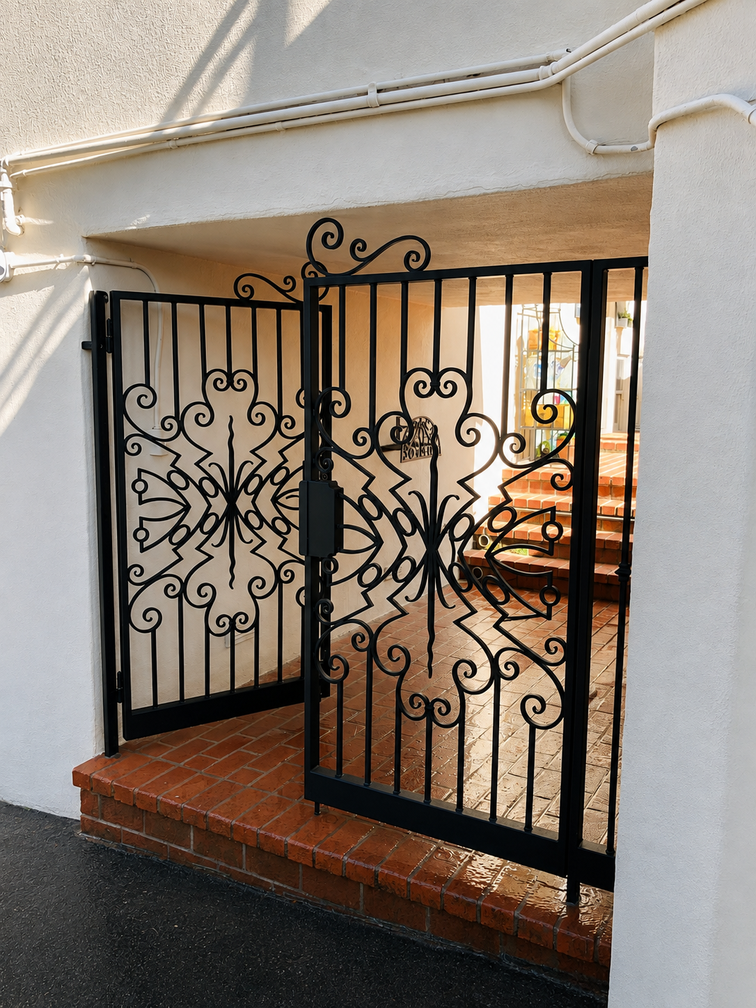 Open black ornamental entry gate with scrollwork under stucco archway