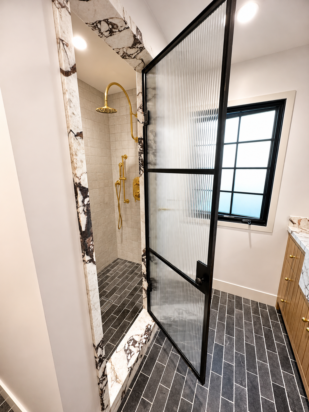 Open black metal and ribbed glass shower door with marble surround