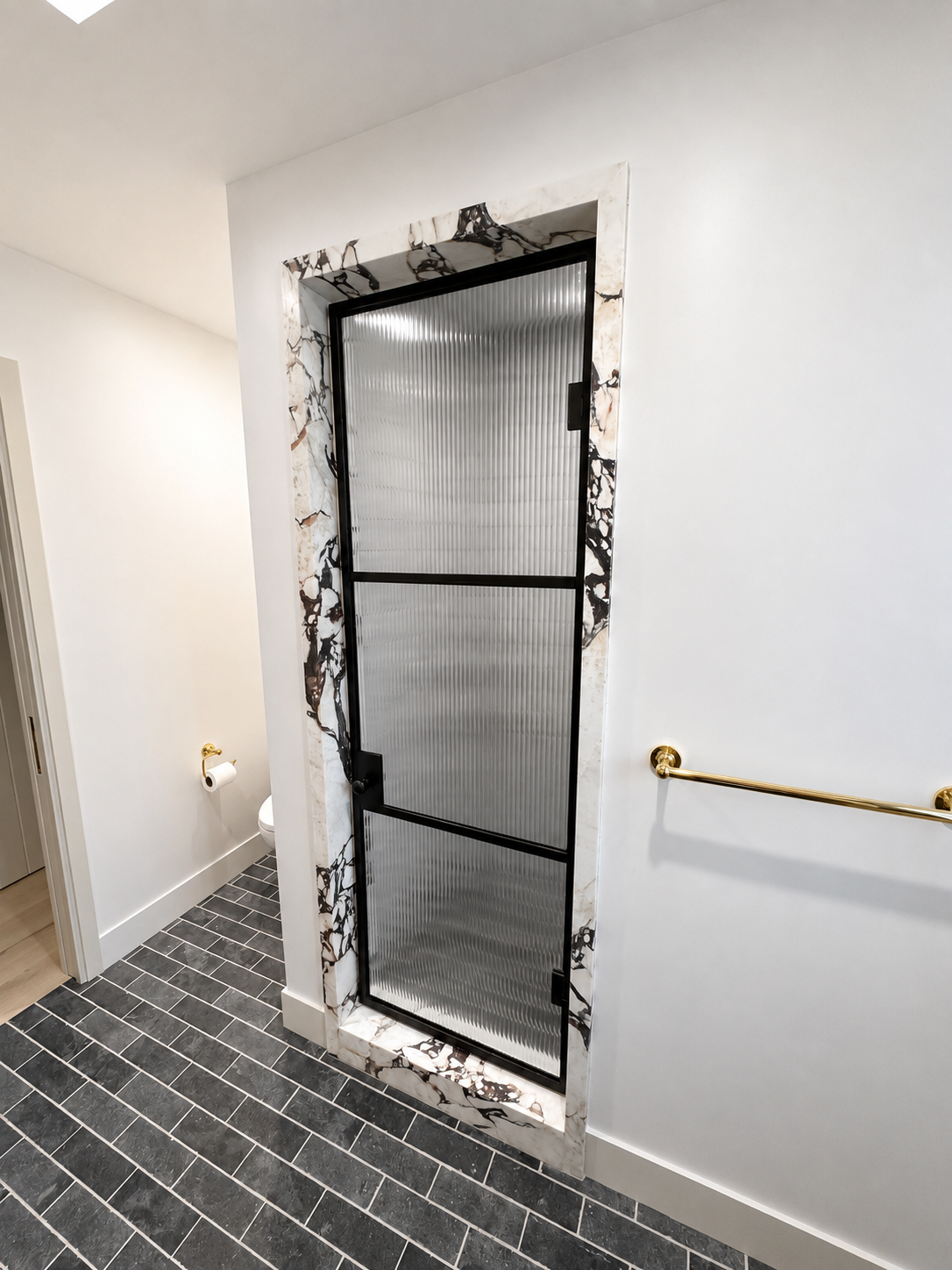Black metal and ribbed glass shower door set in a marble shower opening