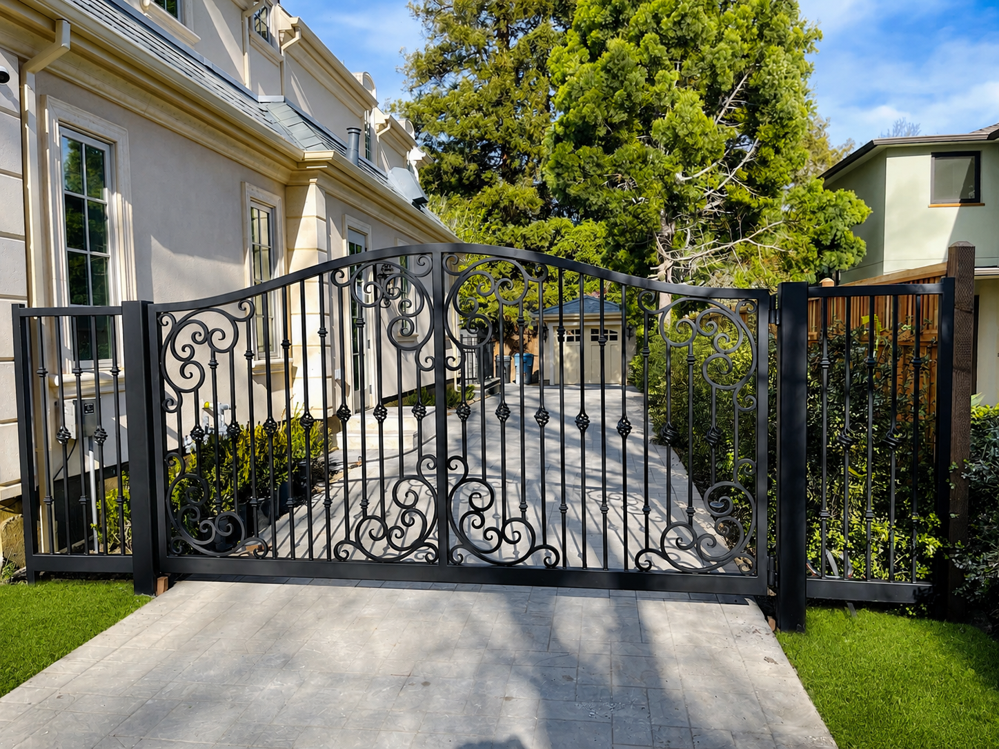 Black ornamental driveway gate with scrollwork in front of stone driveway