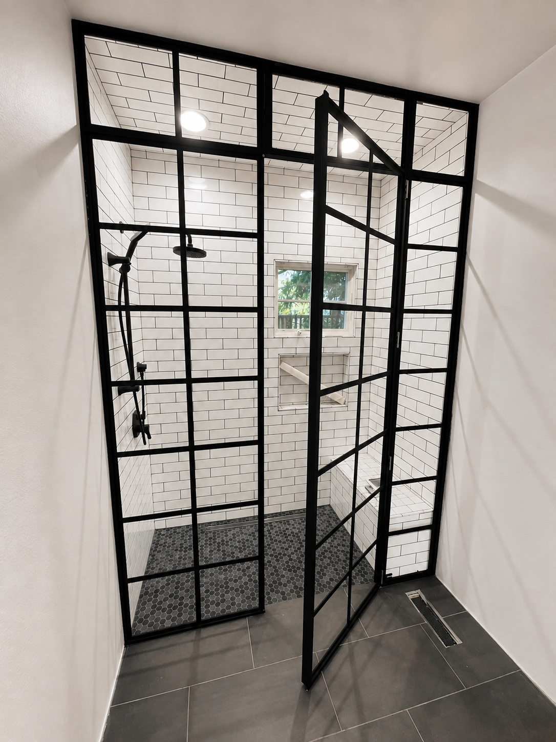Open black grid metal and glass shower door with white tile interior