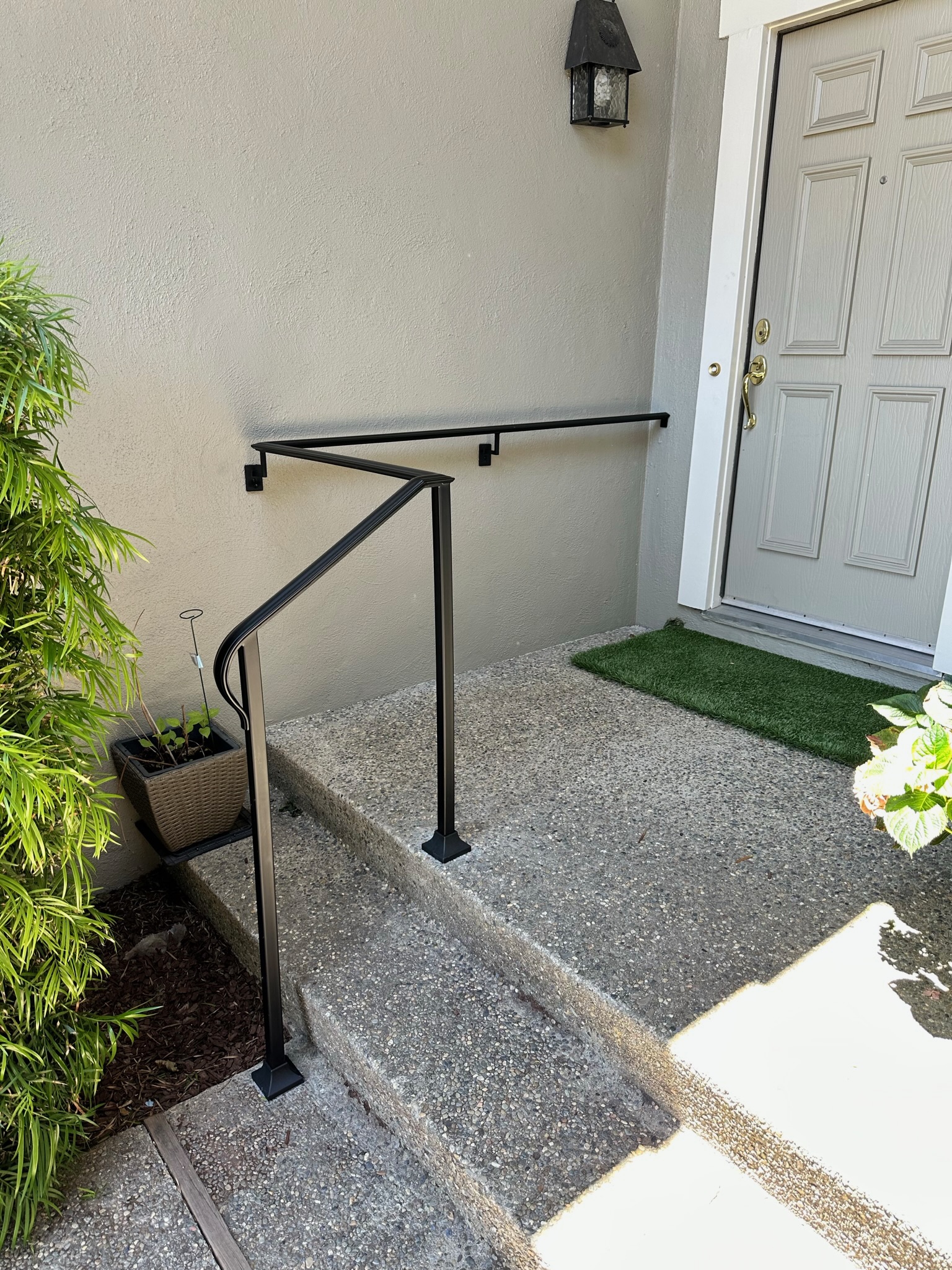 Black entry handrail beside concrete steps and front door