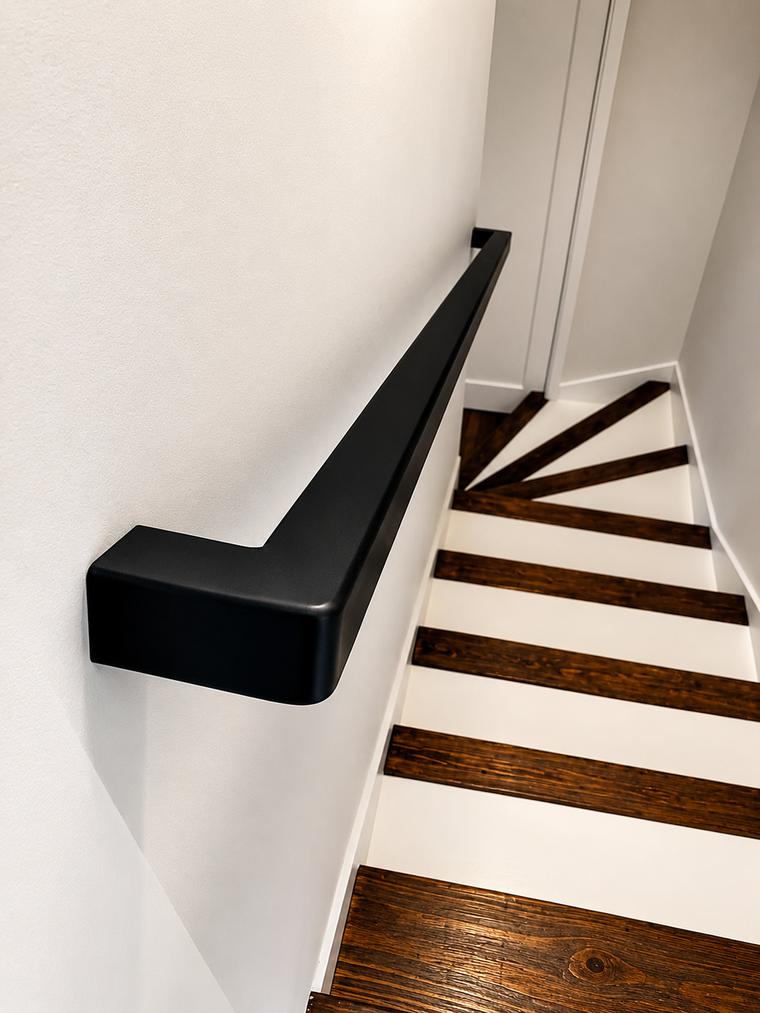 Black wall-mounted stair handrail above wood steps