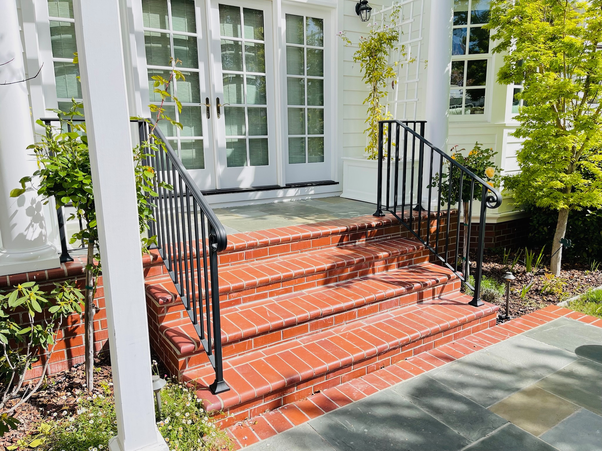Black handrails on red brick entry stairs with white columns