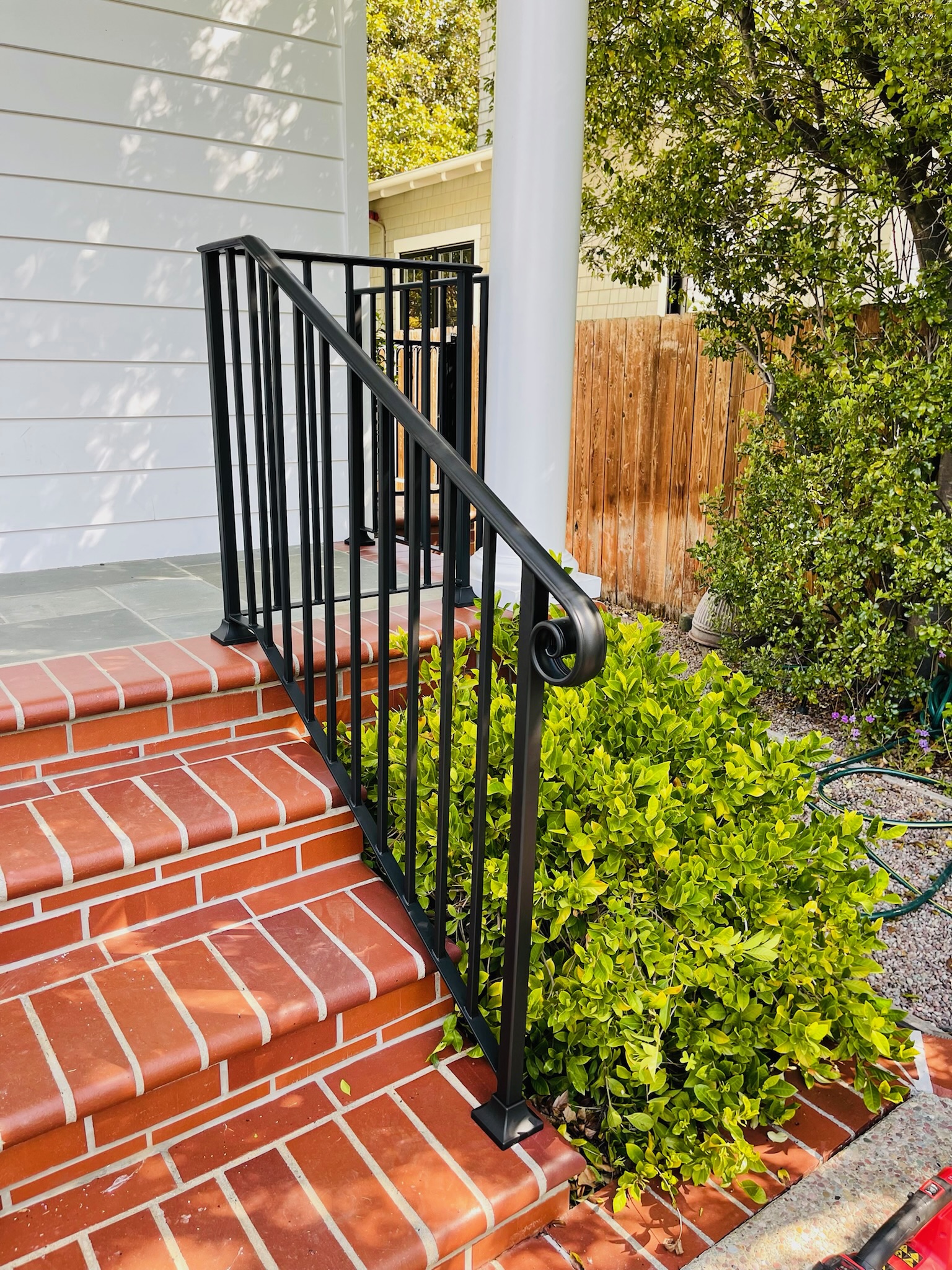 Close side view of black handrail on brick steps beside garden plants