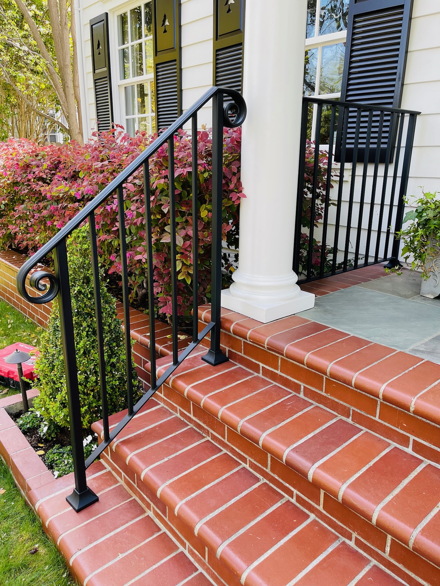 Black handrail with curled end beside white column and brick steps