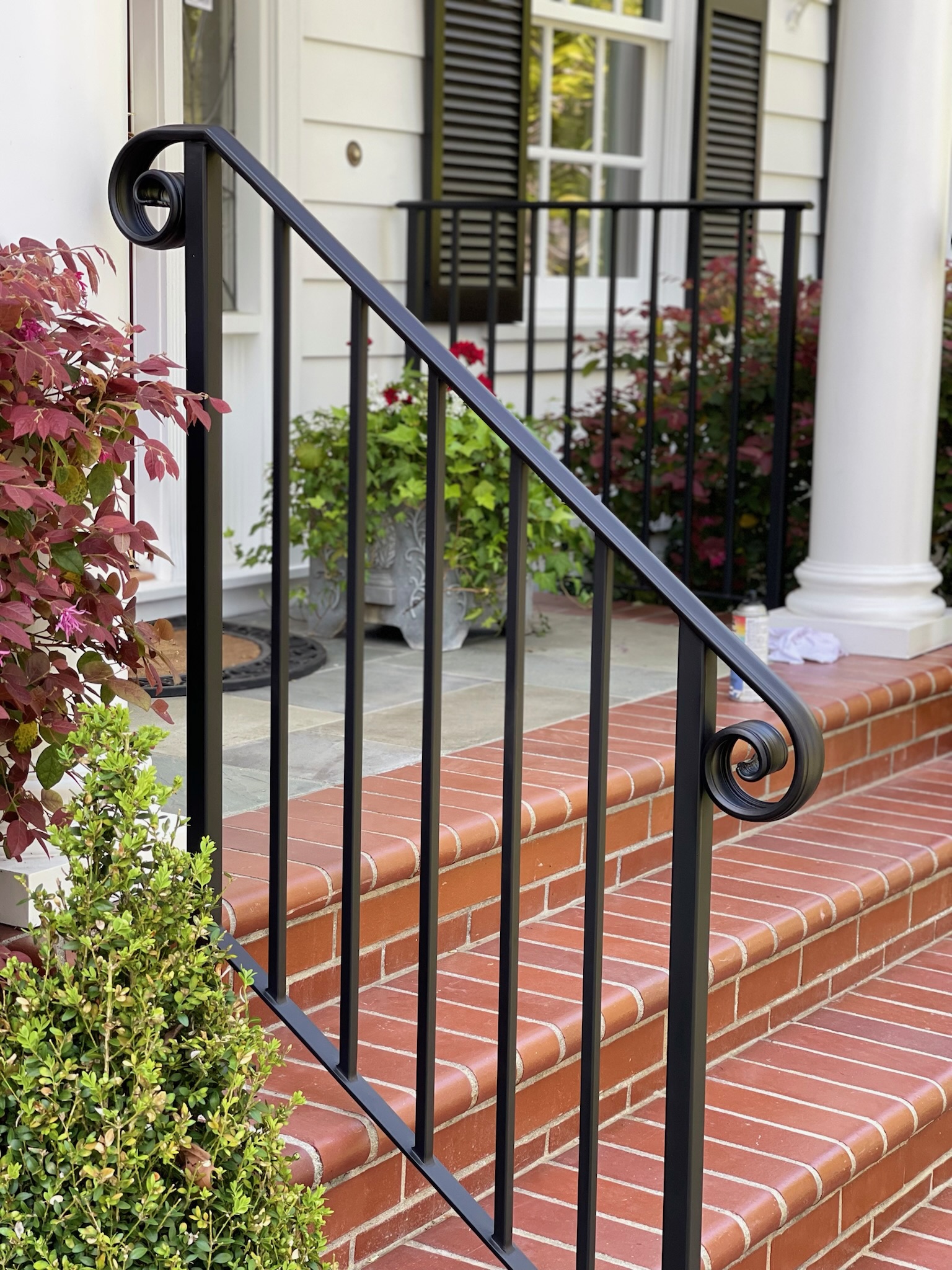 Close detail of black handrail curl over red brick steps