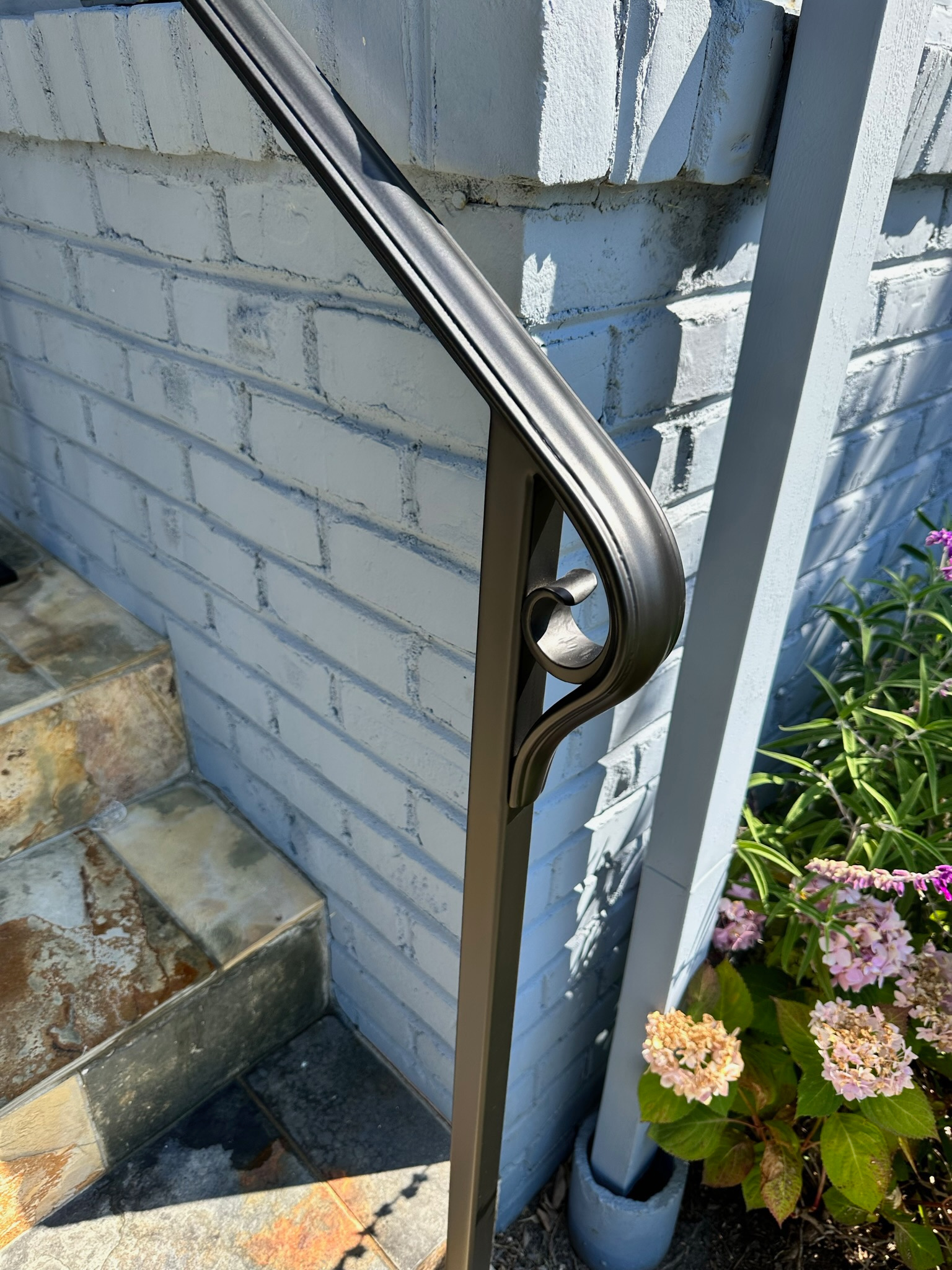 Close detail of bronze entry handrail curve beside white brick wall
