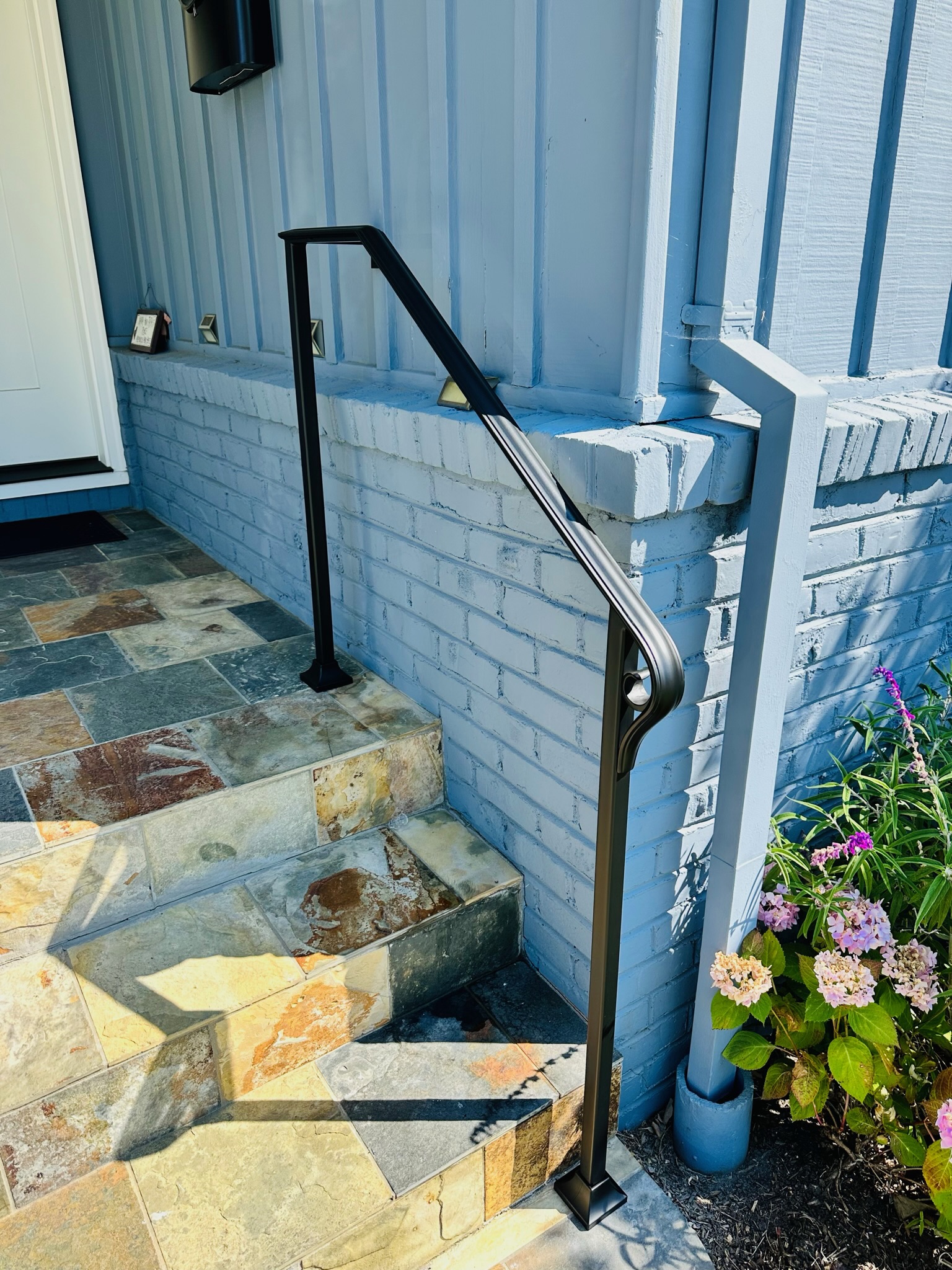 Bronze entry handrail beside stone steps and white brick wall