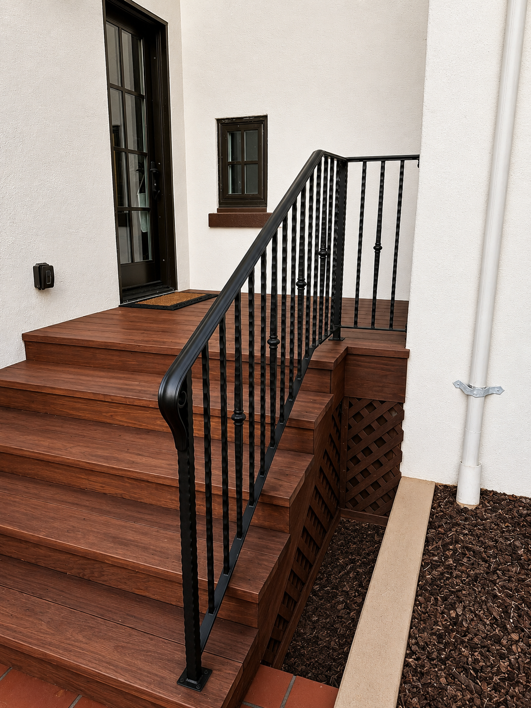Black decorative railing wrapping wood porch steps beside stucco wall