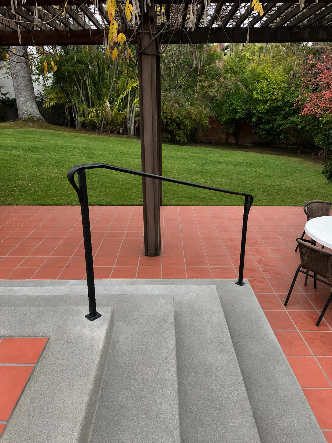 Simple black patio handrail beside concrete steps and red tile floor