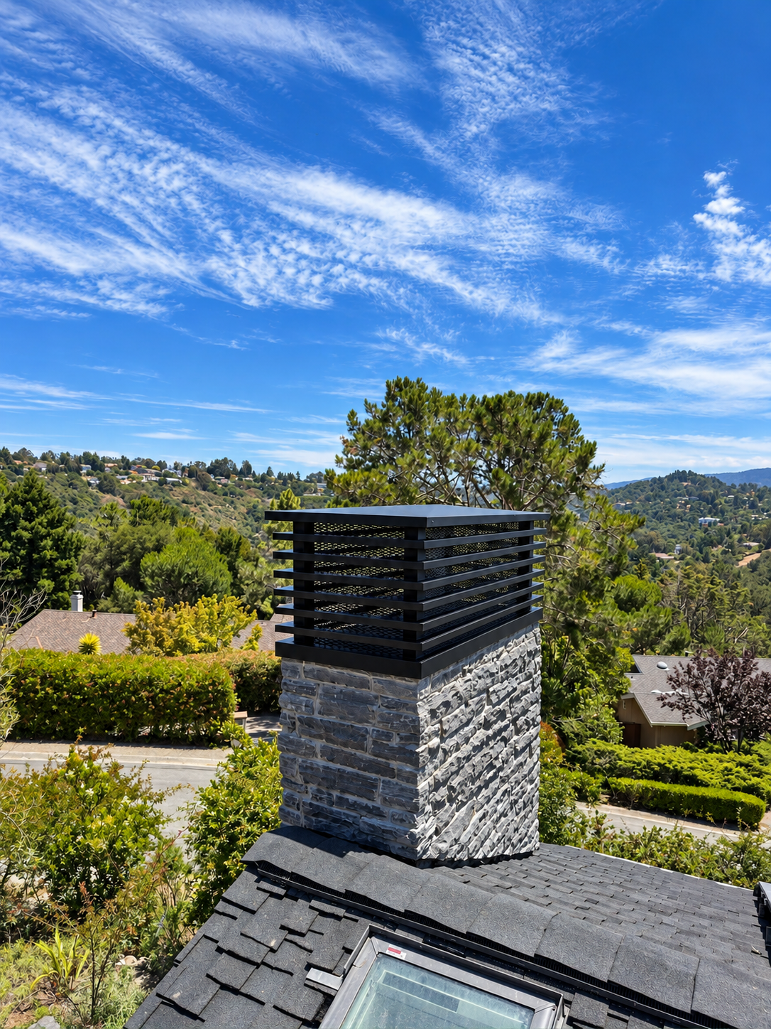 Finished custom metal chimney cap on a stone chimney above a residential roof