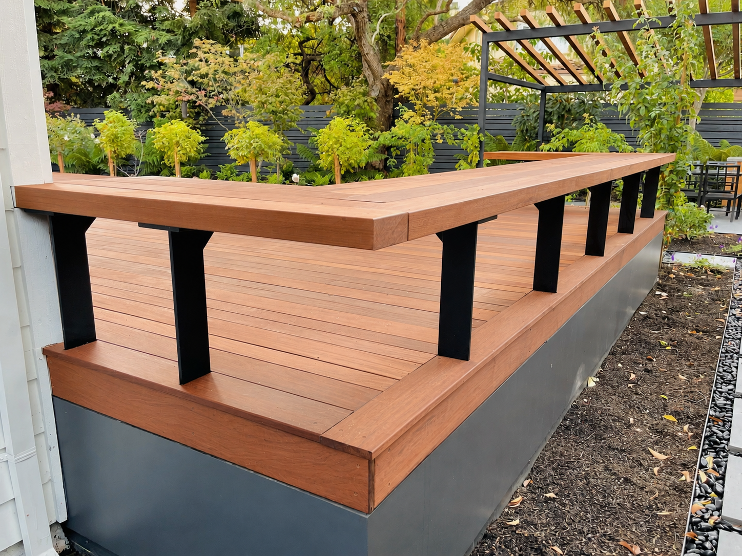 Wood deck with black metal posts and garden pergola in the background