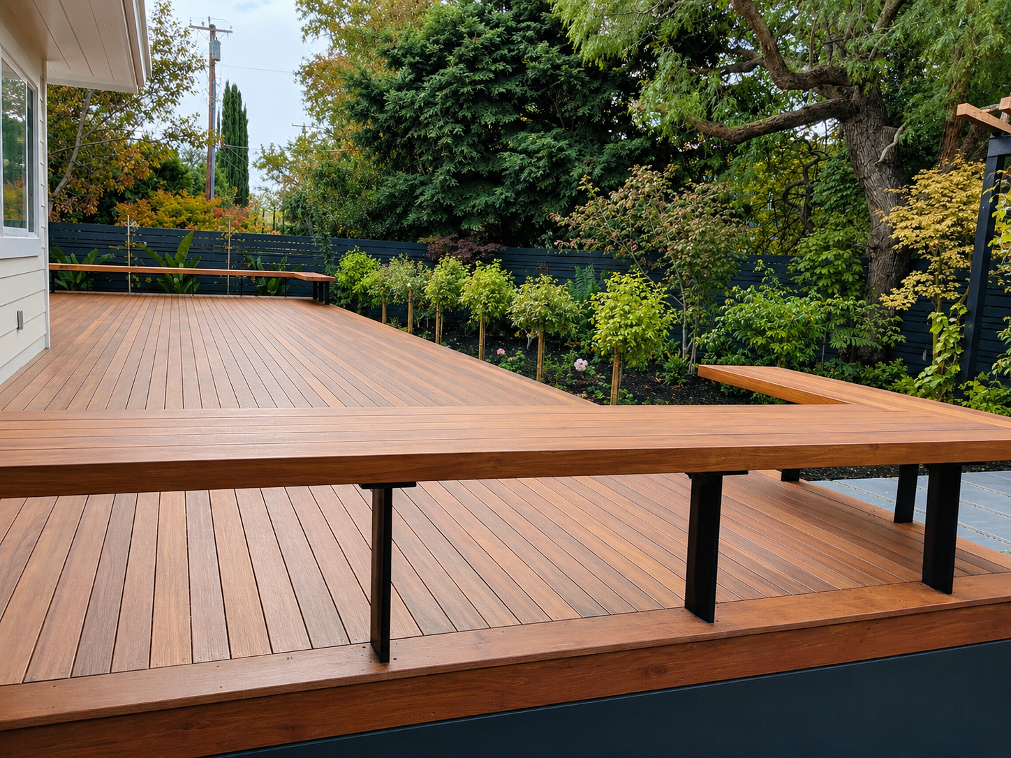 Wide wood deck with black metal supports beside landscaped garden