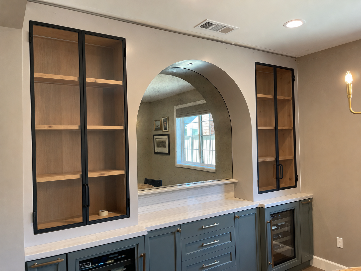 Custom black metal and glass cabinets flanking an arched mirror above a bar counter