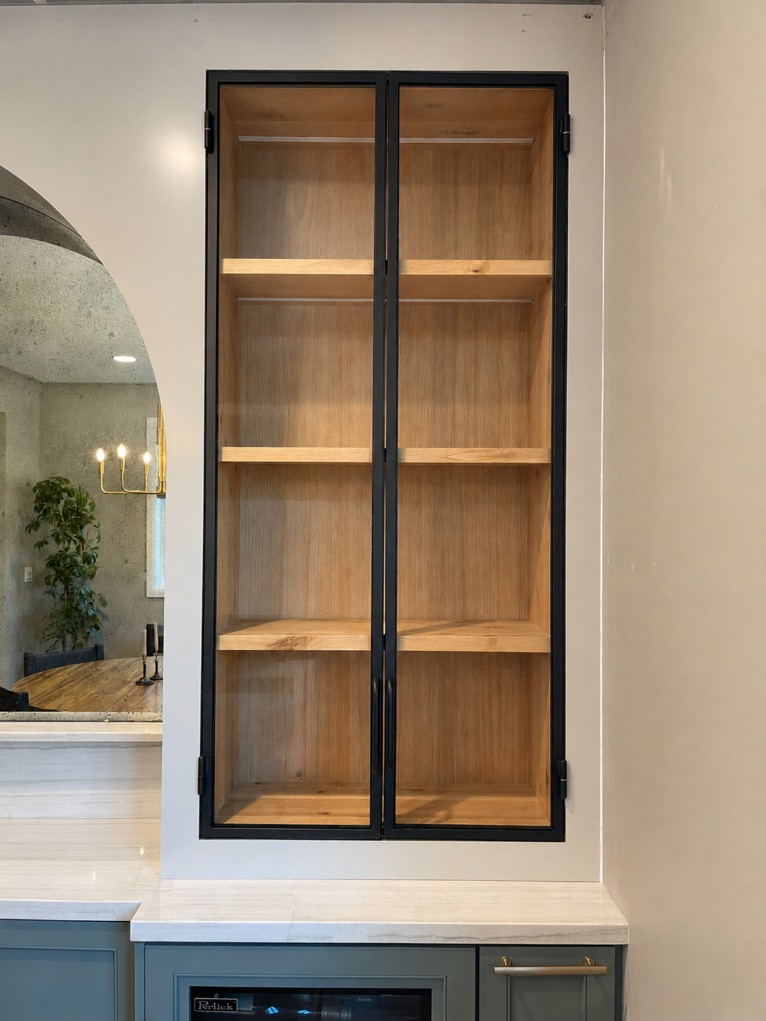 Tall black metal and glass cabinet with wood shelves above a bar counter