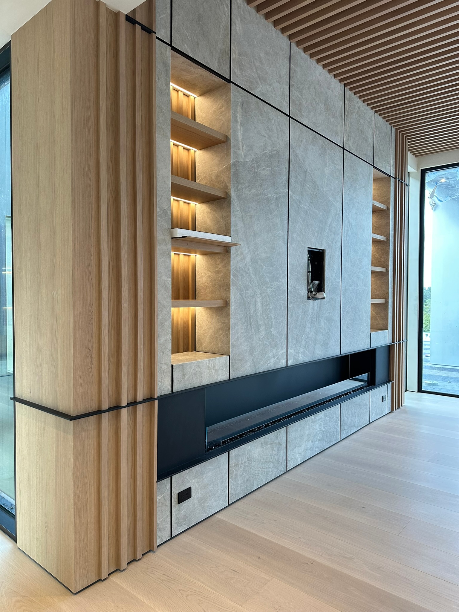 Custom interior media wall with wood slats, stone panels, and black metal trim