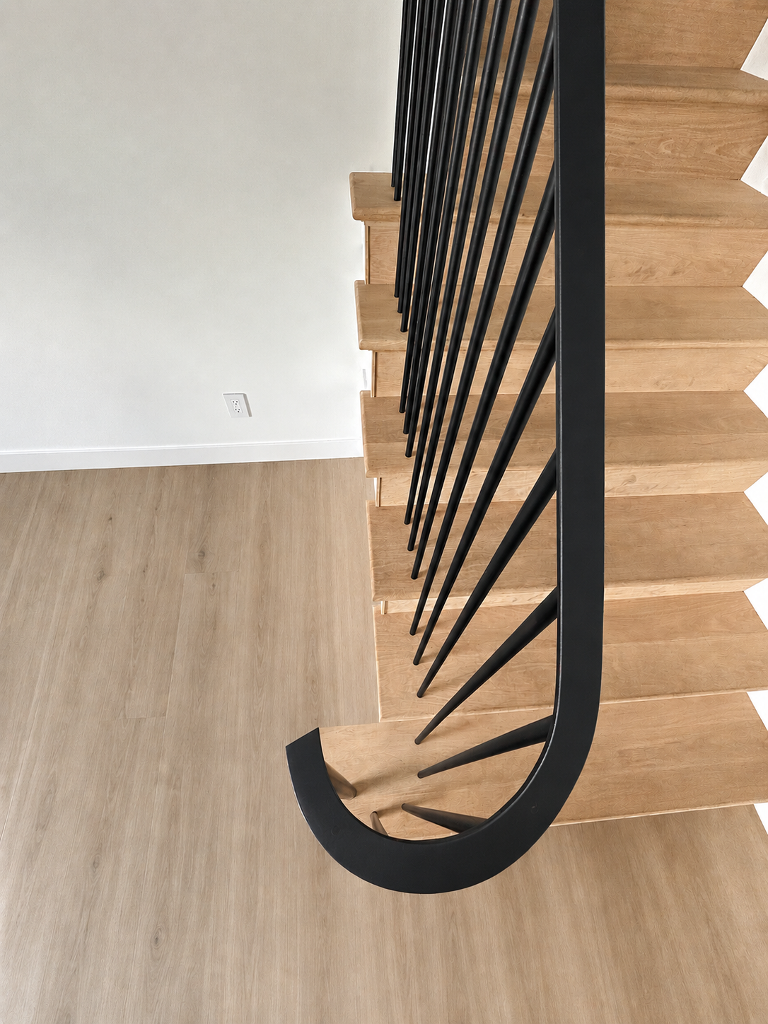 Close-up of curved black railing on light wood stairs