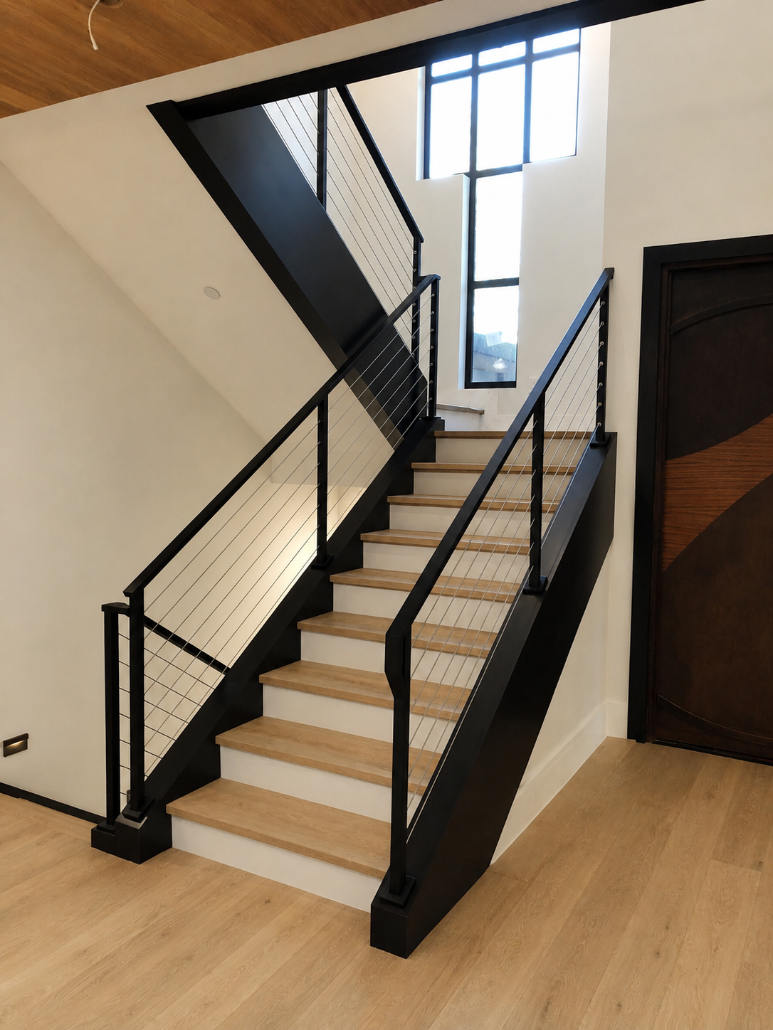 Cable stair railing with black steel stringer and wood treads
