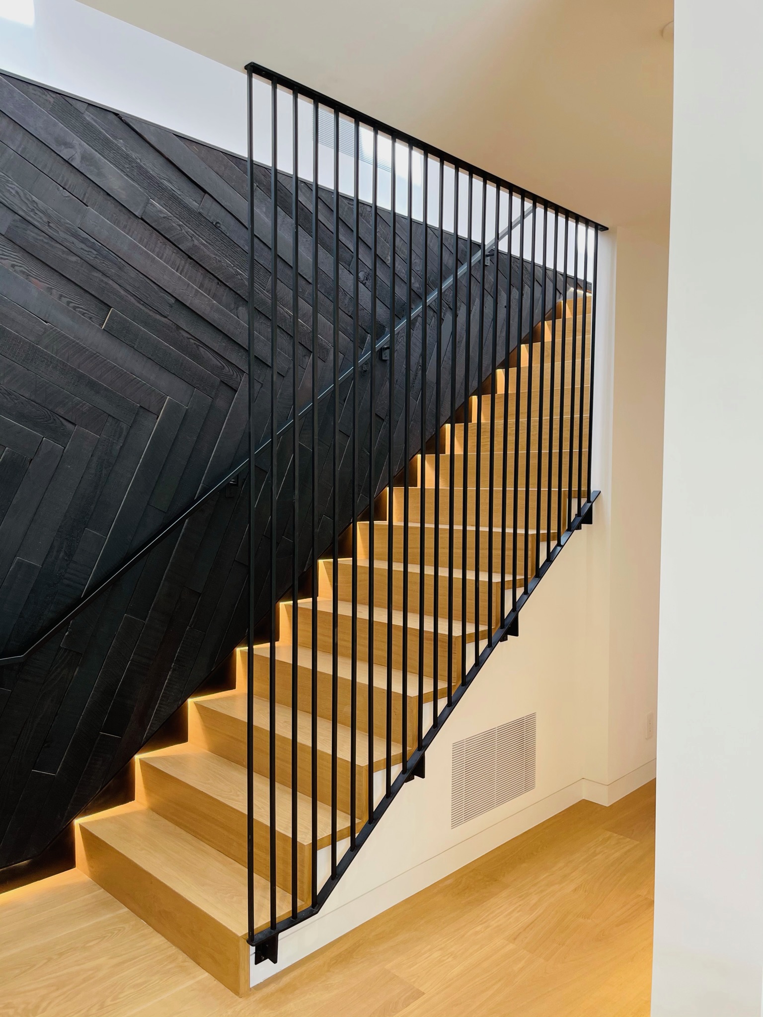 Black vertical stair railing beside light wood steps and dark accent wall