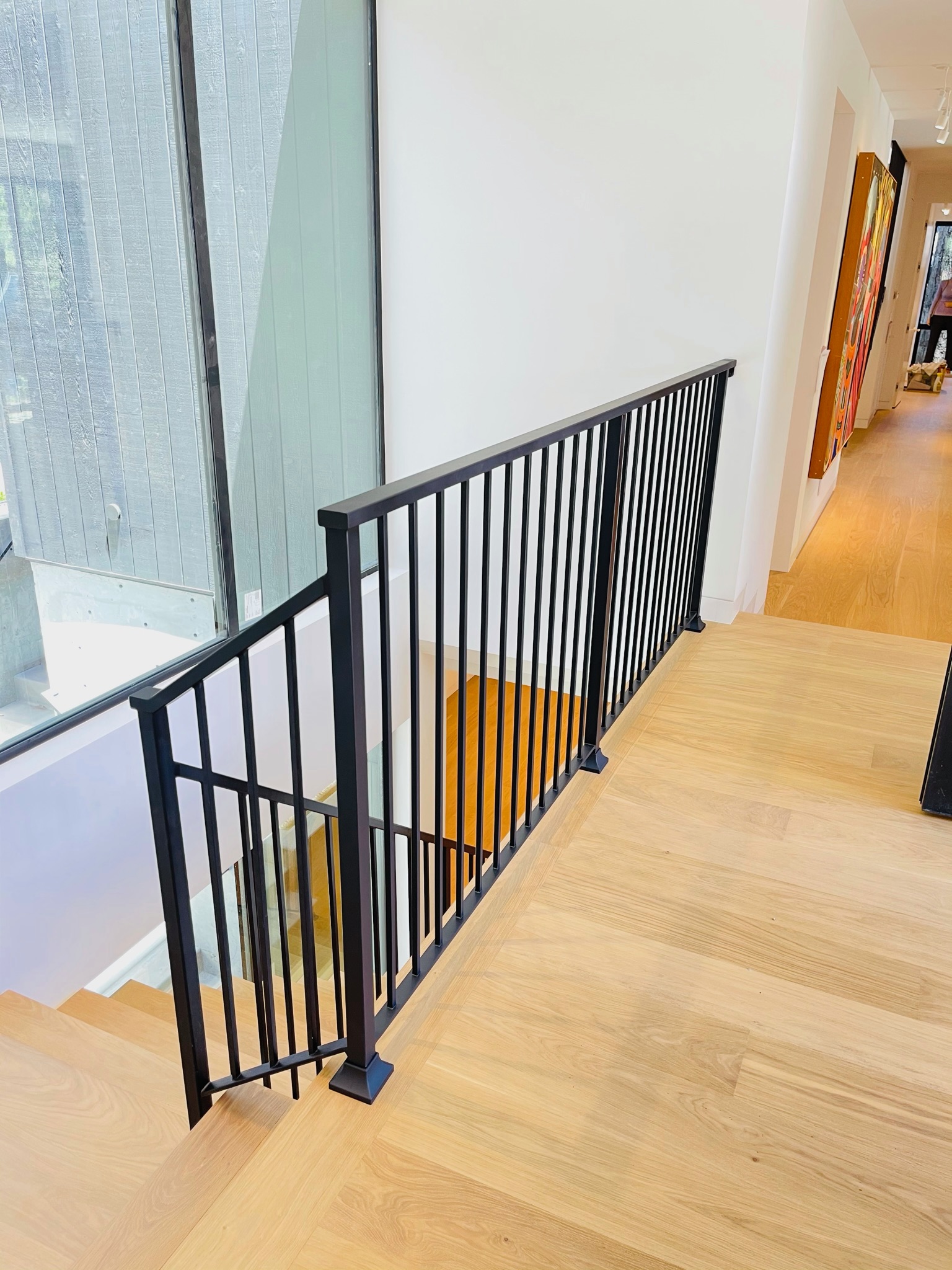 Upper landing black metal railing beside tall window and wood floor