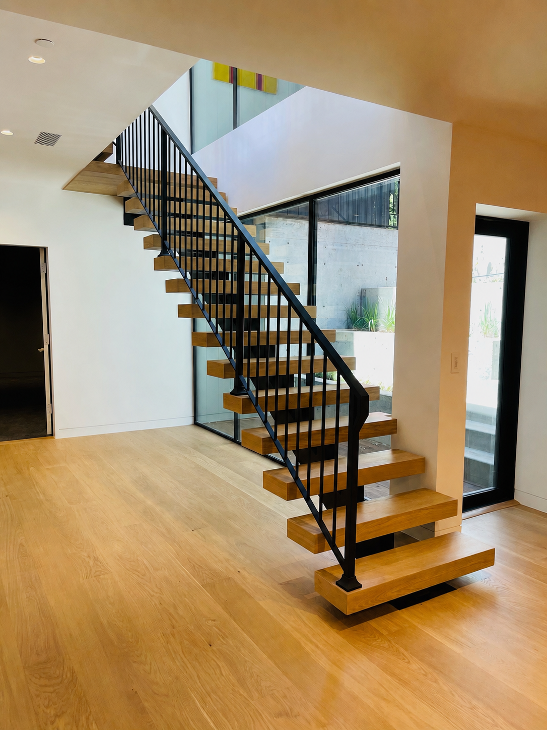 Modern floating wood staircase with black railing in open interior