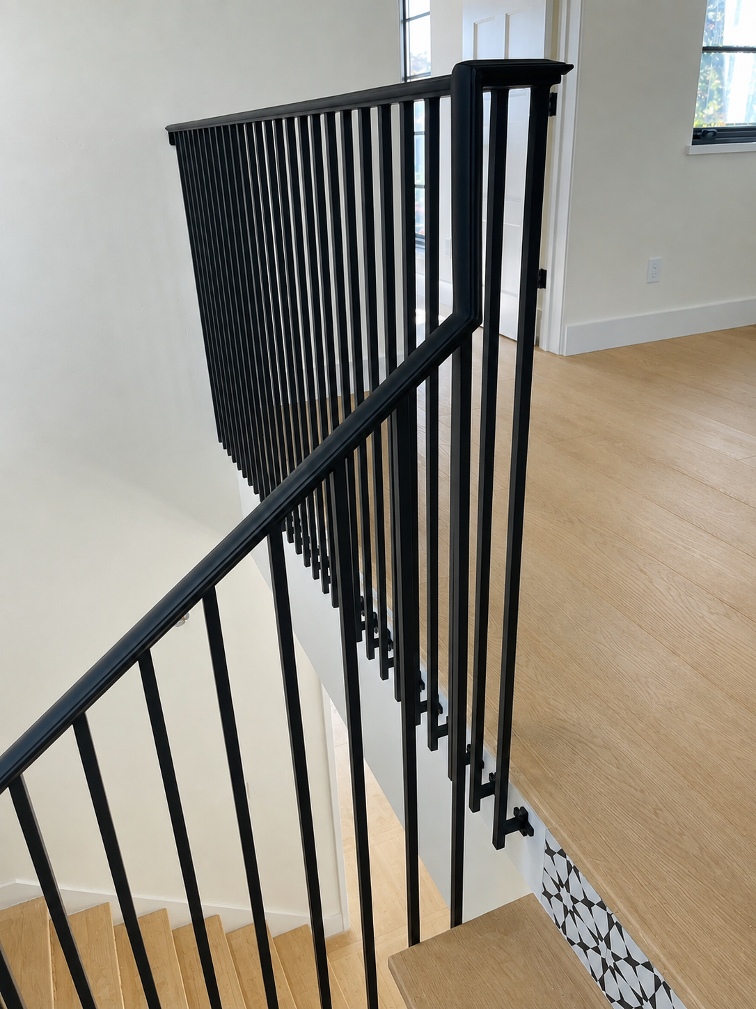 Black stair railing detail beside wood floor and patterned stair risers