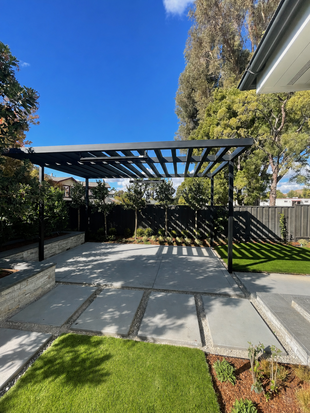 Clean black metal trellis over patio with stepping stones
